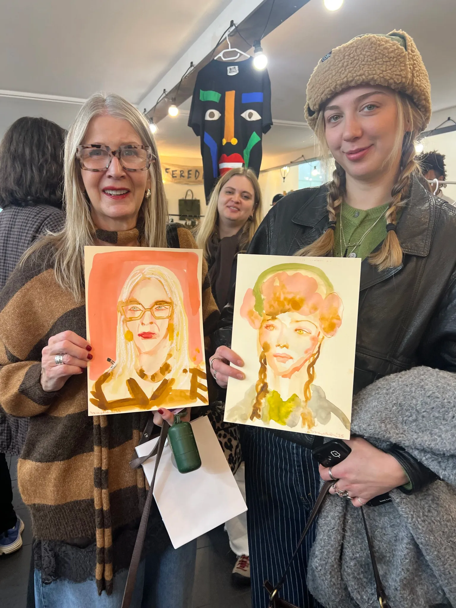 Two women holding up watercolour portraits at a live event by Tracey Smith.