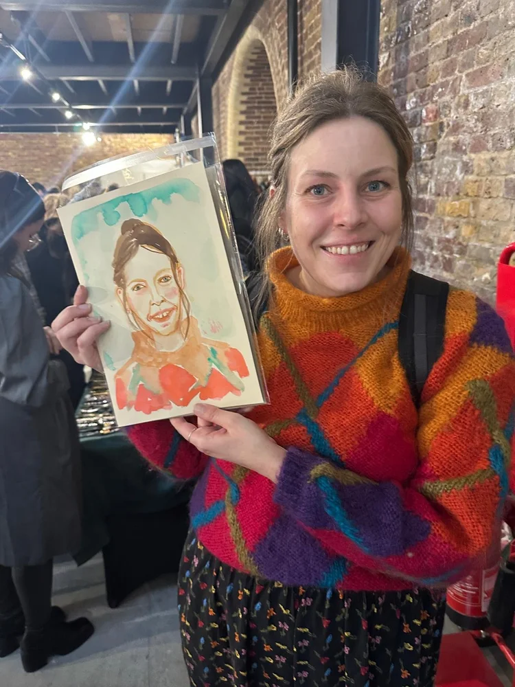 Smiling woman in colourful sweater holding her watercolour portrait by Tracey Smith.